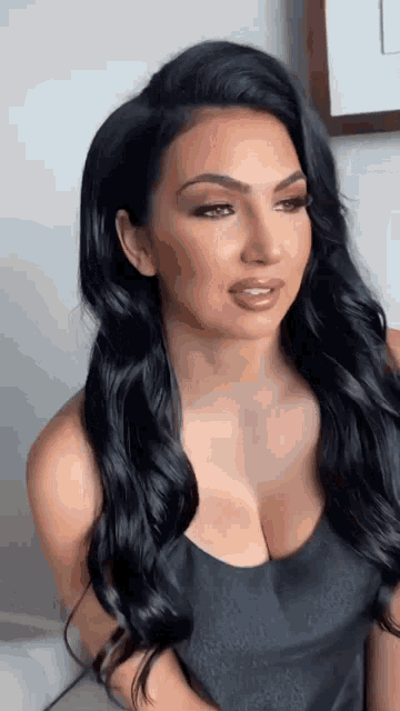 a woman with long black hair is wearing a black tank top with a plunging neckline