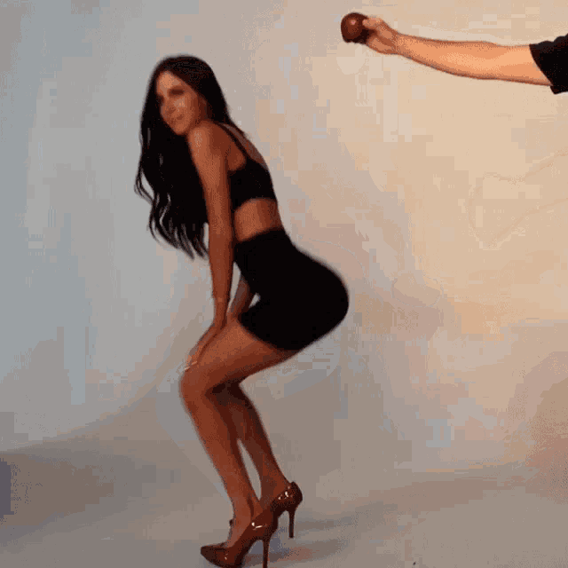 a woman in a black dress and red high heels is squatting in front of a man holding an apple