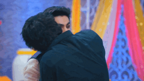 two men are hugging each other in front of a colorful backdrop