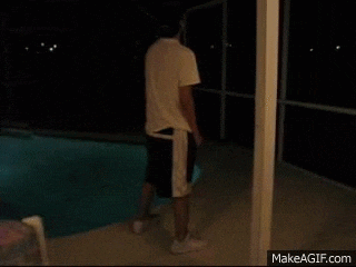 a person is laying on the ground in front of a swimming pool at night .