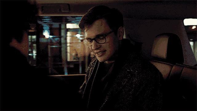 a young man wearing glasses is sitting in the back of a car
