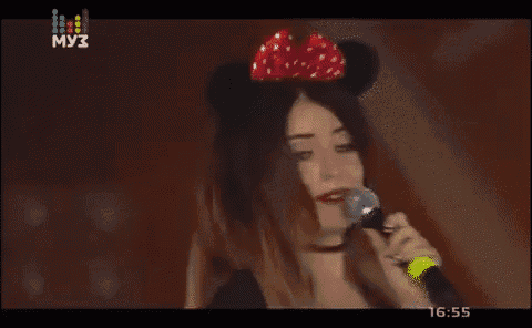 a woman wearing mickey mouse ears singing into a microphone on a tv screen