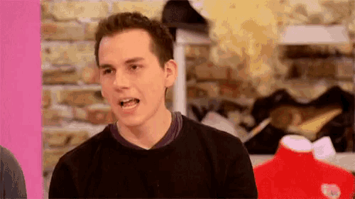 a man in a black sweater is making a funny face while standing in front of a brick wall .