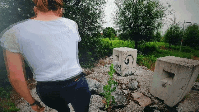 a woman in a white shirt stands in front of a concrete block with the letters gi on it