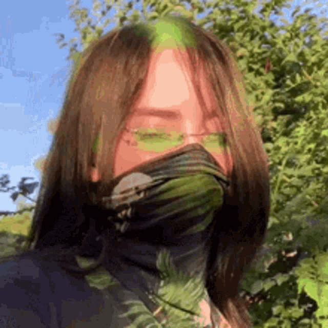 a woman wearing a mask and sunglasses is standing in front of trees .