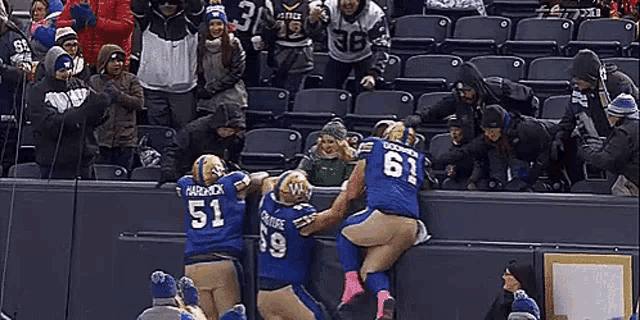 a group of football players are climbing over a wall while fans watch .