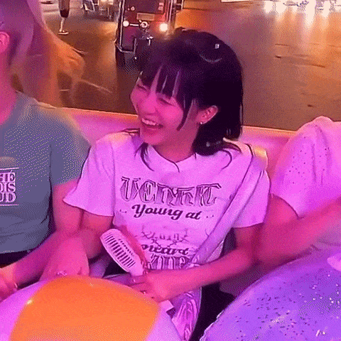 a girl in a white t-shirt is sitting on a couch holding a fan and a beach ball .