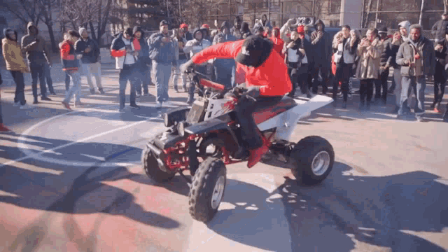 a man in a red sweatshirt is riding a four wheeler in front of a crowd