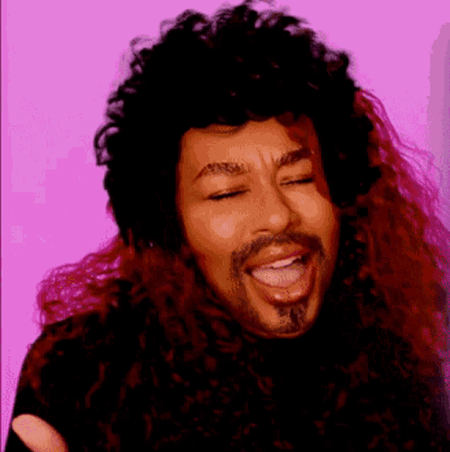 a man with long curly hair and a beard is smiling with his eyes closed