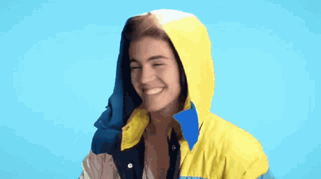 a woman wearing a yellow and blue jacket with a hood smiles