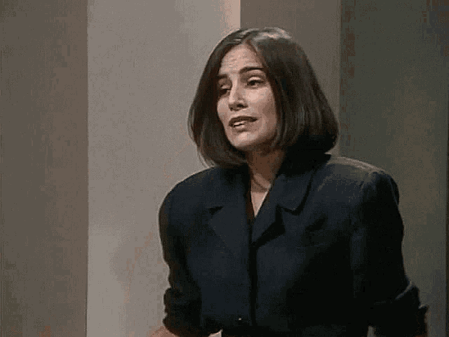 a woman in a black jacket is standing in front of a wall and making a funny face .