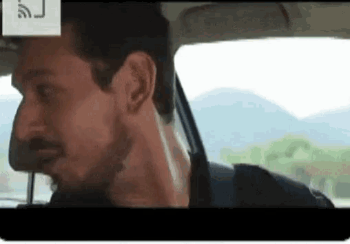 a man with a beard is sitting in a car and looking out the window .