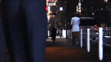 a woman in a white coat walks down a sidewalk next to a car with a license plate that starts with the letter k