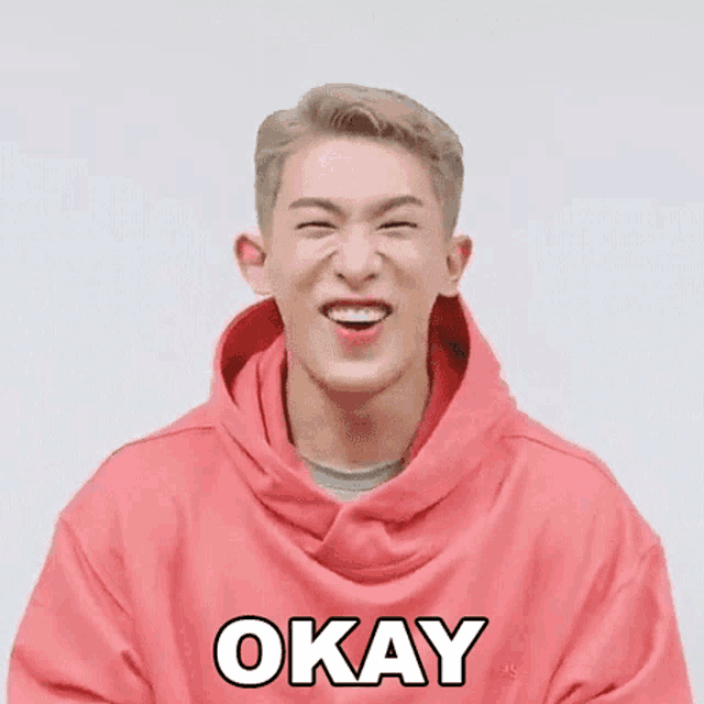 a man in a pink hoodie is smiling and making a face .