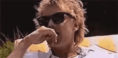a man wearing sunglasses and a mullet is covering his mouth .