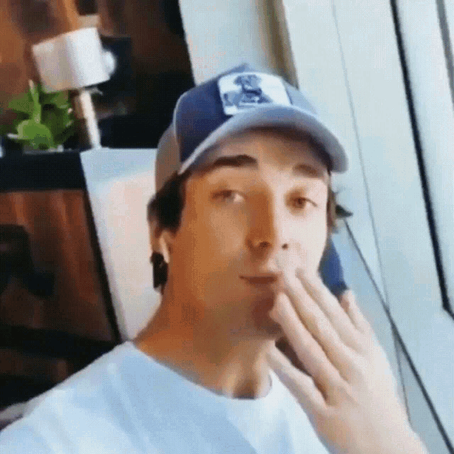 a man wearing a baseball cap is blowing a kiss
