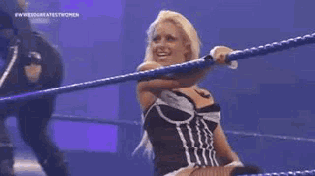 a woman is standing in a wrestling ring holding a rope and smiling .