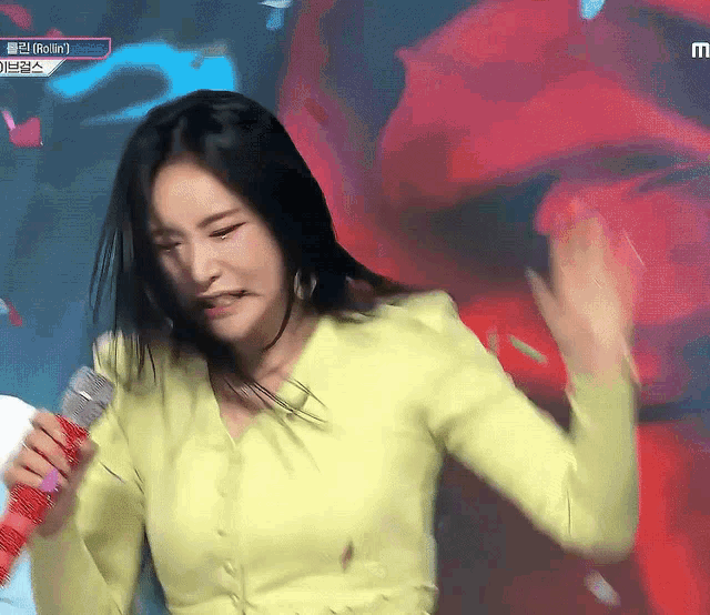 a woman in a yellow shirt is holding a microphone and making a face