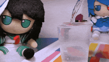 two stuffed dolls sit on a table with a cup of water being poured into them