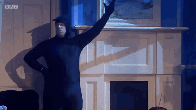 a man in a black bodysuit is standing in front of a fireplace with bbc written on the door