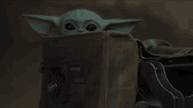 a baby yoda looks out from behind a piece of cloth