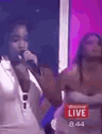 a woman is singing into a microphone on a stage in front of a live audience .