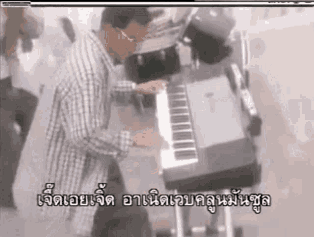 a man in a plaid shirt is playing a piano in a video with foreign writing