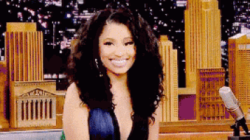 a woman with curly hair and a plunging neckline is smiling in front of a city skyline .