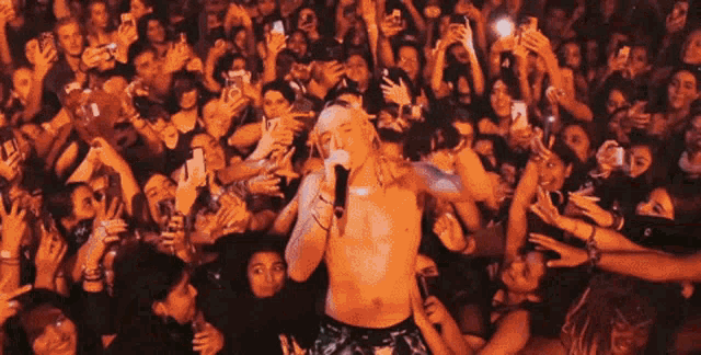 a shirtless man sings into a microphone in front of a crowd