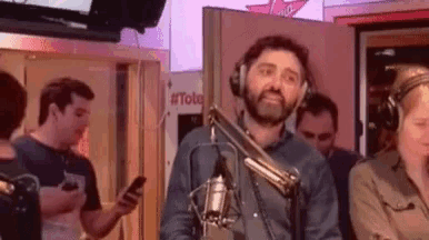 a man wearing headphones is standing in front of a microphone in a studio .