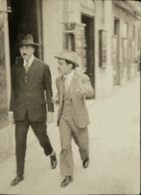 two men in suits and hats walk down a street