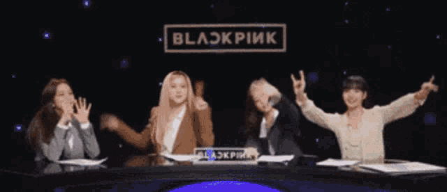 a group of women sitting in front of a blackpink sign