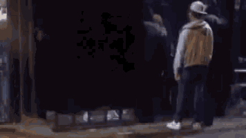 a man in a hat is walking down a dark street at night .