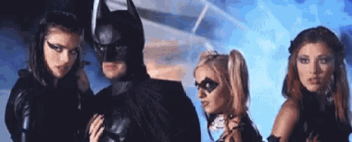 a man in a batman costume is standing next to two women dressed as batman and harley quinn .