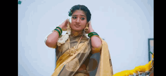 a woman in a yellow saree is putting a garland on her head .