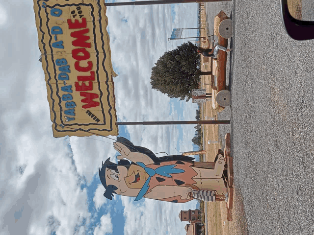 a welcome sign for yabba-dab-a-do with a flintstone statue in front of it