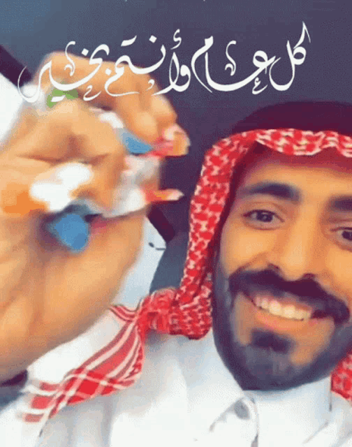 a man wearing a white shirt and a red and white scarf is smiling with arabic writing behind him
