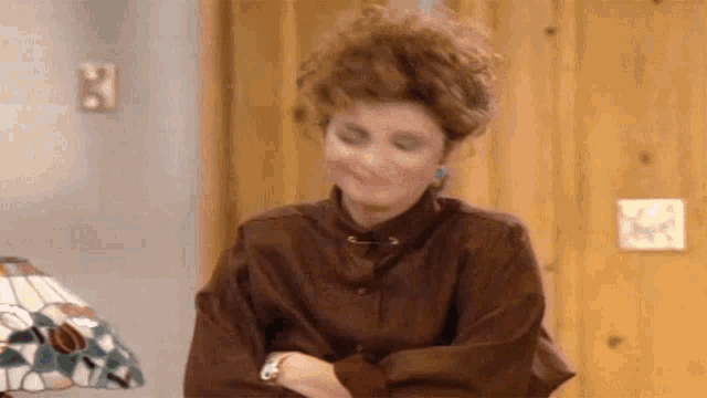 a woman in a brown shirt is sitting at a table with her hands on her hips .