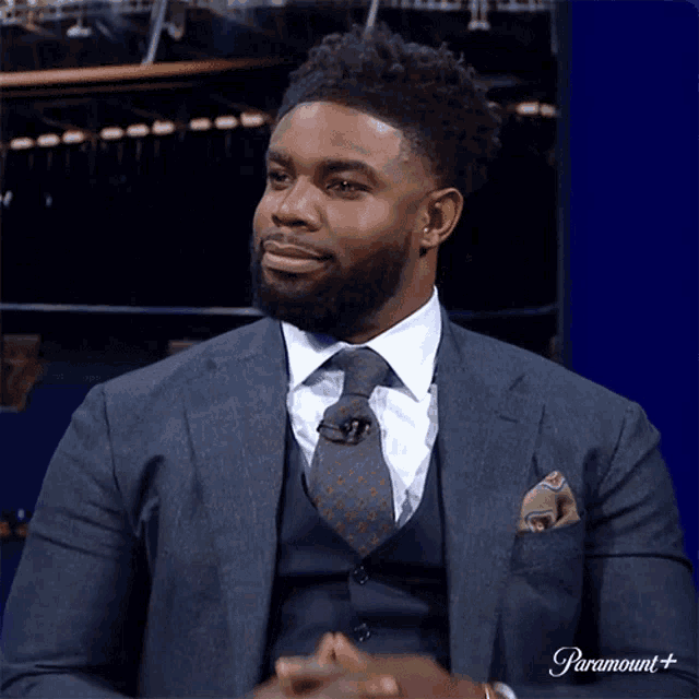a man in a suit and tie is sitting in front of a screen that says paramount +