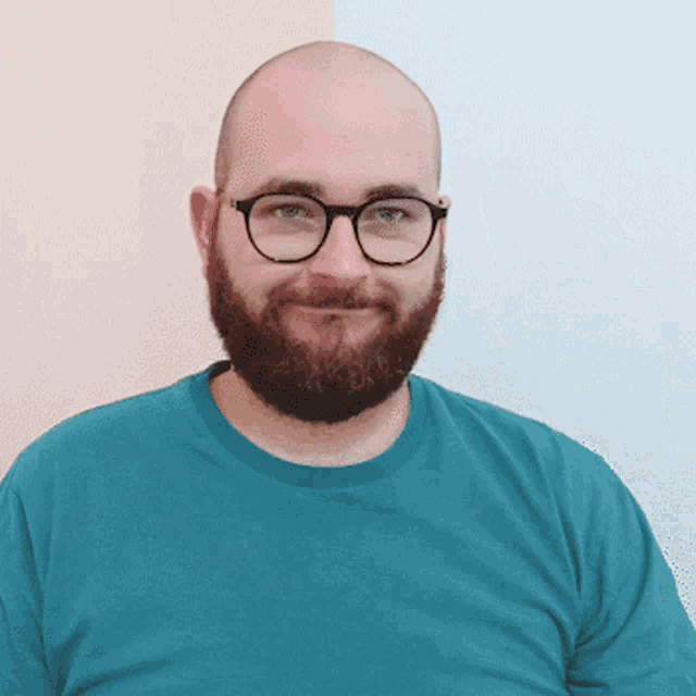 a man with glasses and a beard is smiling and waving his hand