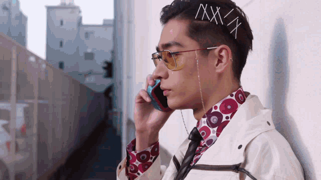 a man wearing sunglasses and a shirt with circles on it talks on a cell phone