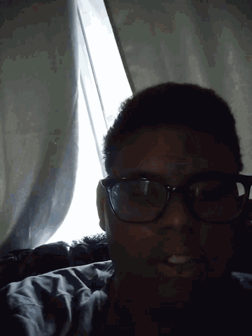 a man wearing glasses is smiling and looking out a window
