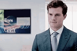 a man in a suit and tie is standing in front of a painting that says grey .