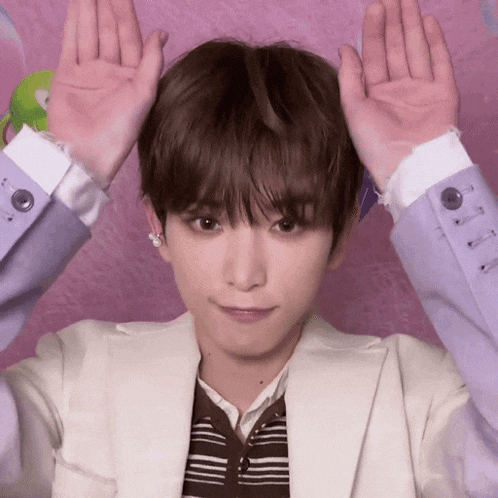 a young man wearing a purple jacket is making a funny face with his hands up .