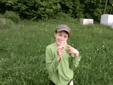 a boy in a green shirt is holding a dandelion in his hands