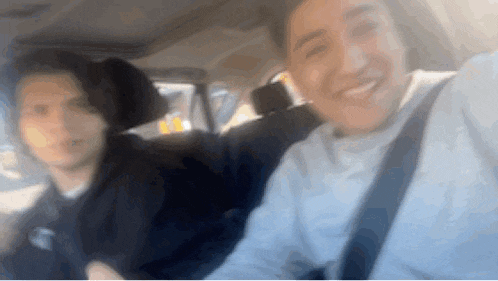 two young men are sitting in the back seat of a car .