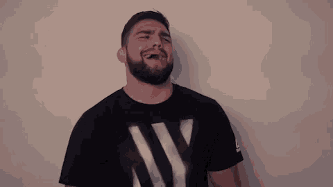 a man with a beard is wearing a black t-shirt with a white letter w on it .