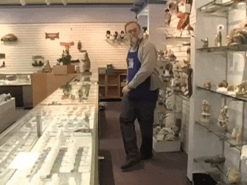 a man in a blue apron is standing in front of a display case in a store .