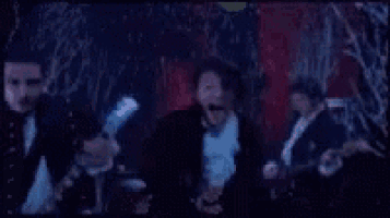 a man in a tuxedo is playing a guitar in front of a table .