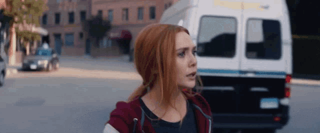 a woman with red hair is walking down a street next to a white van .